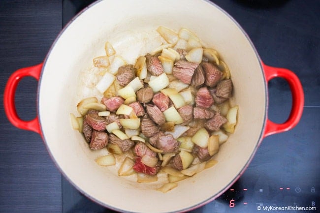 Stir frying onions and diced beef in a pot.