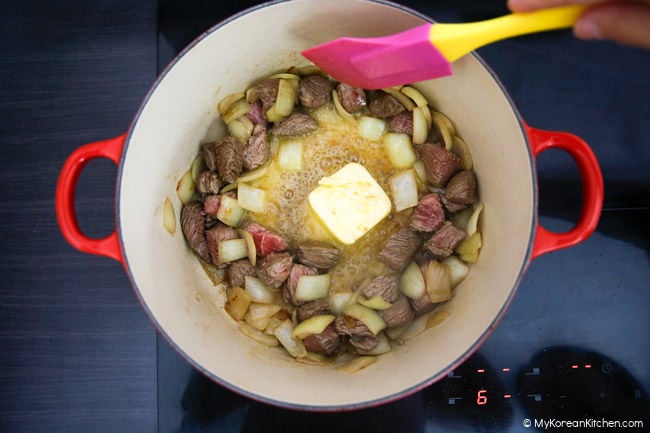 Melting butter in a pot of cooked onions and diced beef.
