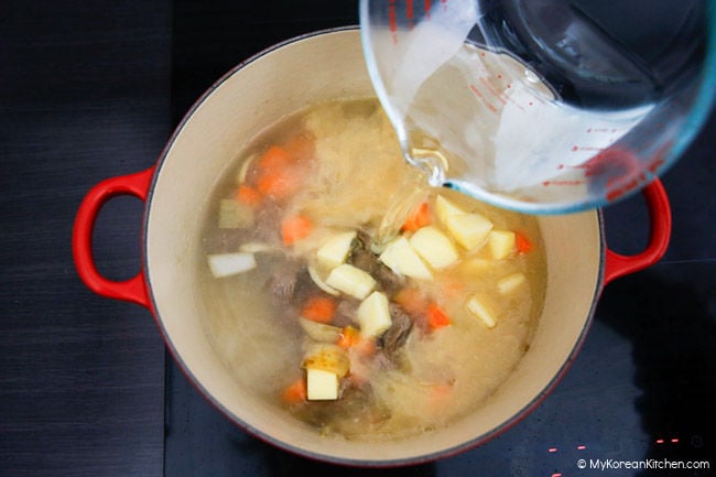 Pouring water over a pot of vegetables and meat.