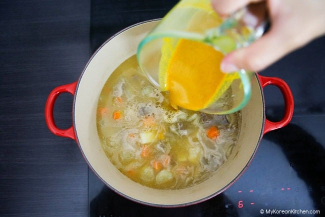 Pouring curry dissolved in water over a pot of boiled vegetables.
