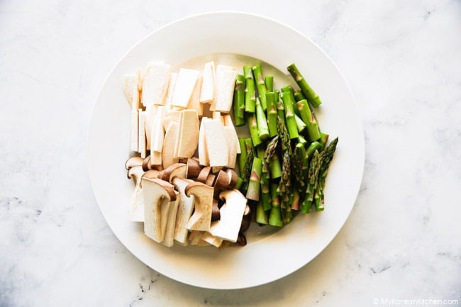 Plate with sliced king oyster mushrooms and chopped asparagus.