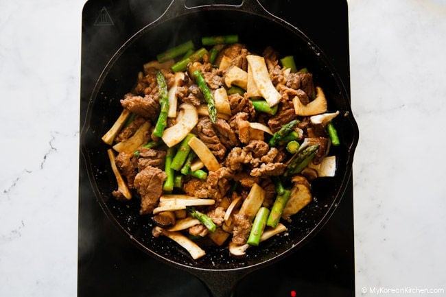 Stir-frying BBQ pork with mushrooms and asparagus in a skillet.