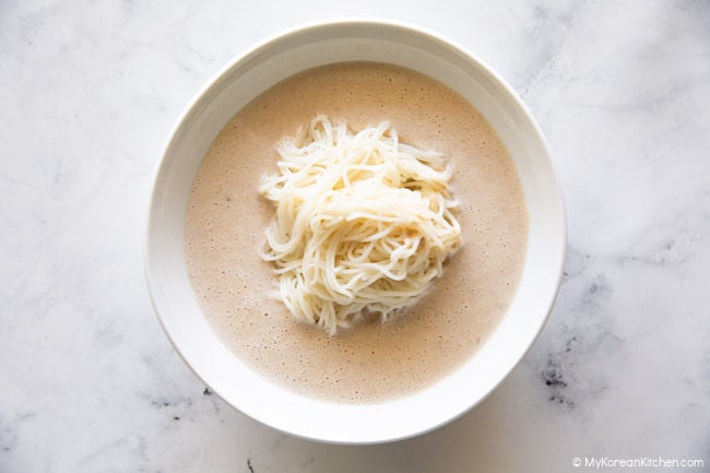 Somen noodles served in a white bowl with soy milk soup being poured in.