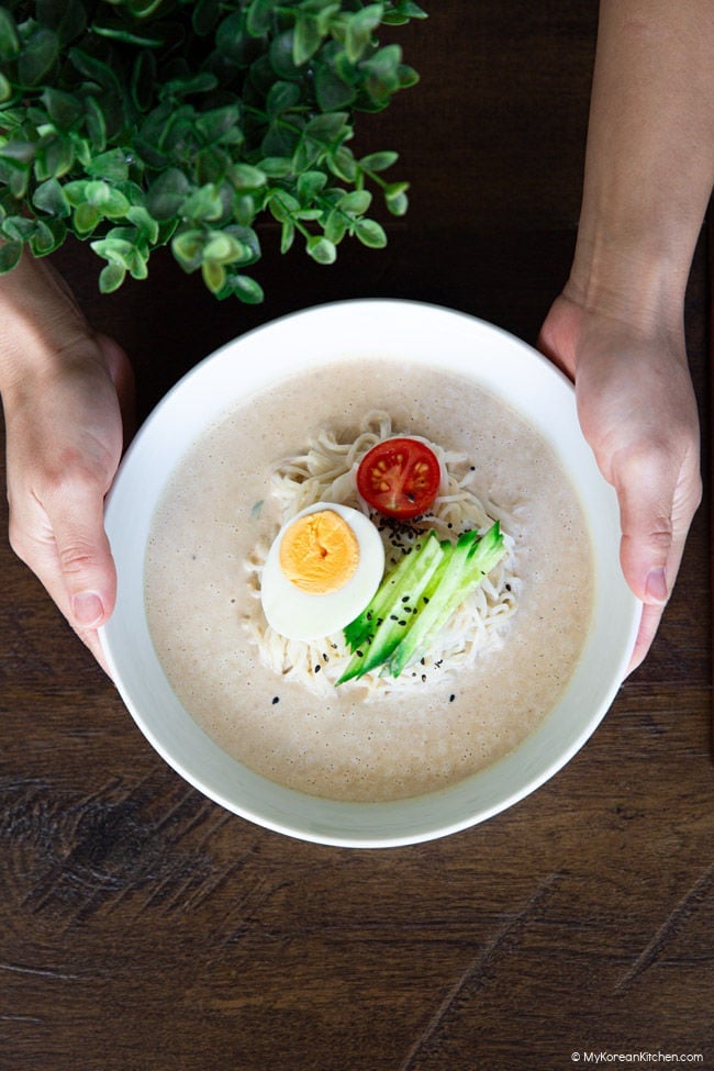 Holding a bowl of kongguksu with both hands over a wooden table.