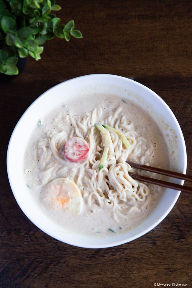 Kongguksu mixed with toppings and soy milk noodle soup using chopsticks.