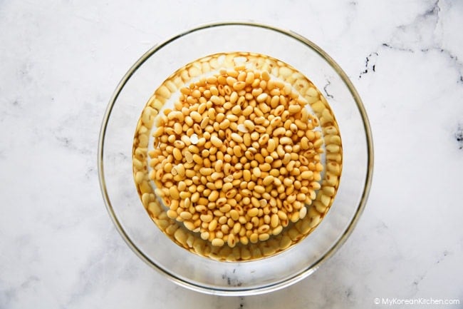 Dried soybeans soaking in water in a clear bowl.