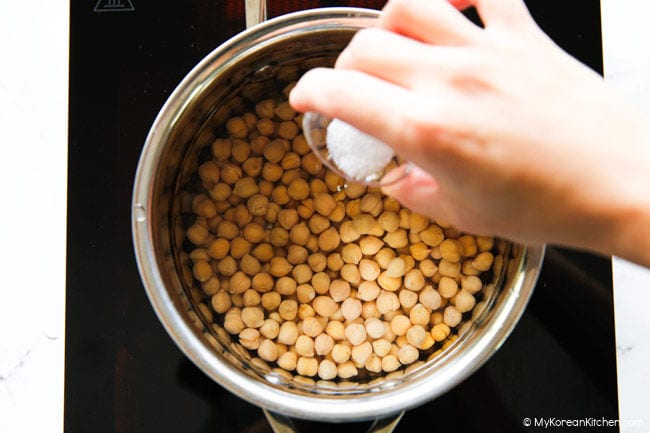 Chickpeas boiling in a pot with salt being added.