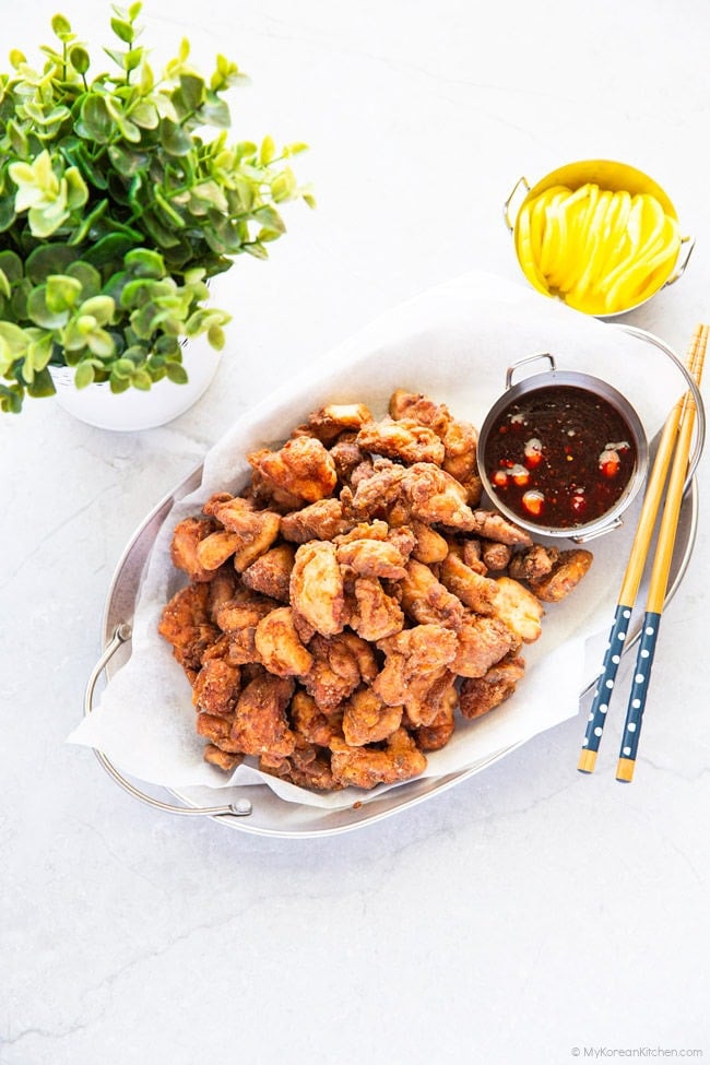 Deep-fried chicken on an oval tray with a bowl of sauce and a pair of chopsticks.