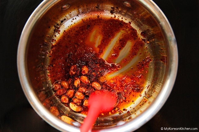 Stir-frying peanuts and chili flakes in chili oil.