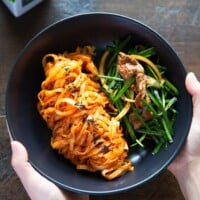 Holding a black bowl of spicy knife-cut noodles and brisket salad with garlic chives.