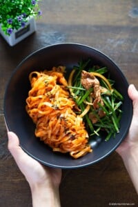 Holding a black bowl of spicy knife-cut noodles and brisket salad with garlic chives.