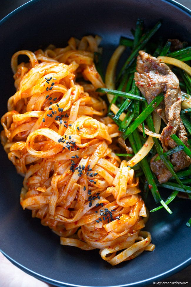 Spicy knife-cut noodles and brisket salad with garlic chives in a black bowl.