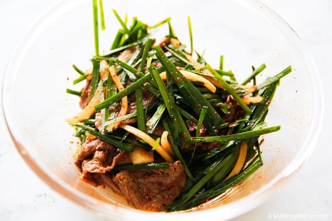 Korean brisket salad with garlic chives and sweet, spicy, tangy dressing in a mixing bowl.