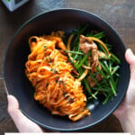 Holding a black bowl of spicy knife-cut noodles and brisket salad with garlic chives.