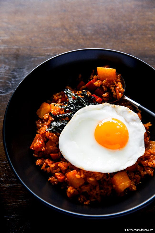 Radish kimchi and spam fried rice served in a shallow bowl. Sunny side egg is on top of the rice.