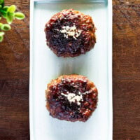 Two tteokgalbi on a rectangular plate placed on a wooden bench.