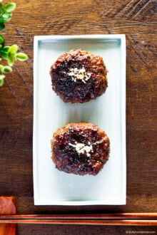 Two tteokgalbi on a rectangular plate placed on a wooden bench.