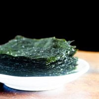 Roasted seaweed placed on a white plate on wooden benchtop.