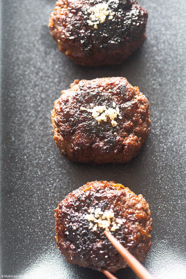 Three pan-fried tteokgalbi patties on a black rectangular plate.