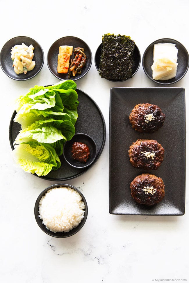 A spread of Korean dishes featuring a bowl of rice, Tteokgalbi, and assorted side dishes like kimchi.