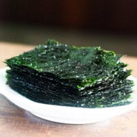 Roasted seaweed placed on a white plate on wooden benchtop.