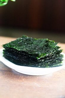 Roasted seaweed placed on a white plate on wooden benchtop.