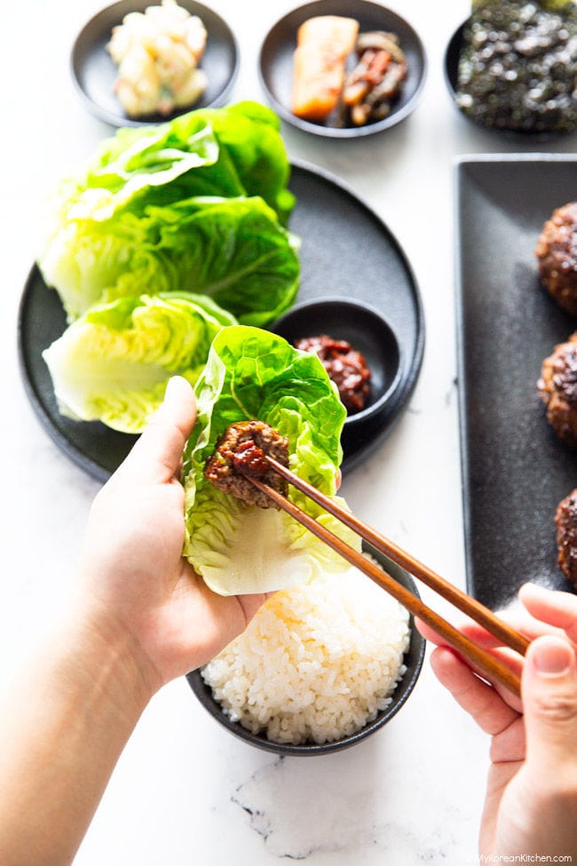 A bite-sized Tteokgalbi on lettuce with ssamjang, placed by wooden chopsticks.