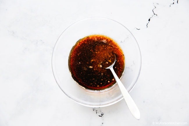 Ingredients for Tteokgalbi sauce in a clear glass bowl, ready to be mixed with a spoon.