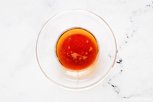 Sesame and perilla oils mixed in a small clear bowl on a white countertop.