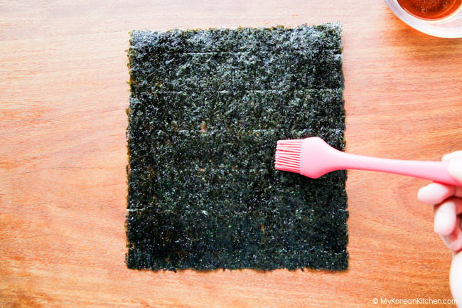 Applying oil with a silicone brush to dried seaweed on a wooden cutting board.