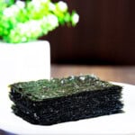 Roasted seaweed placed on a white plate on wooden benchtop.