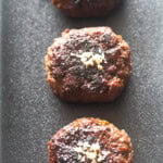 Three pan-fried tteokgalbi patties on a black rectangular plate.