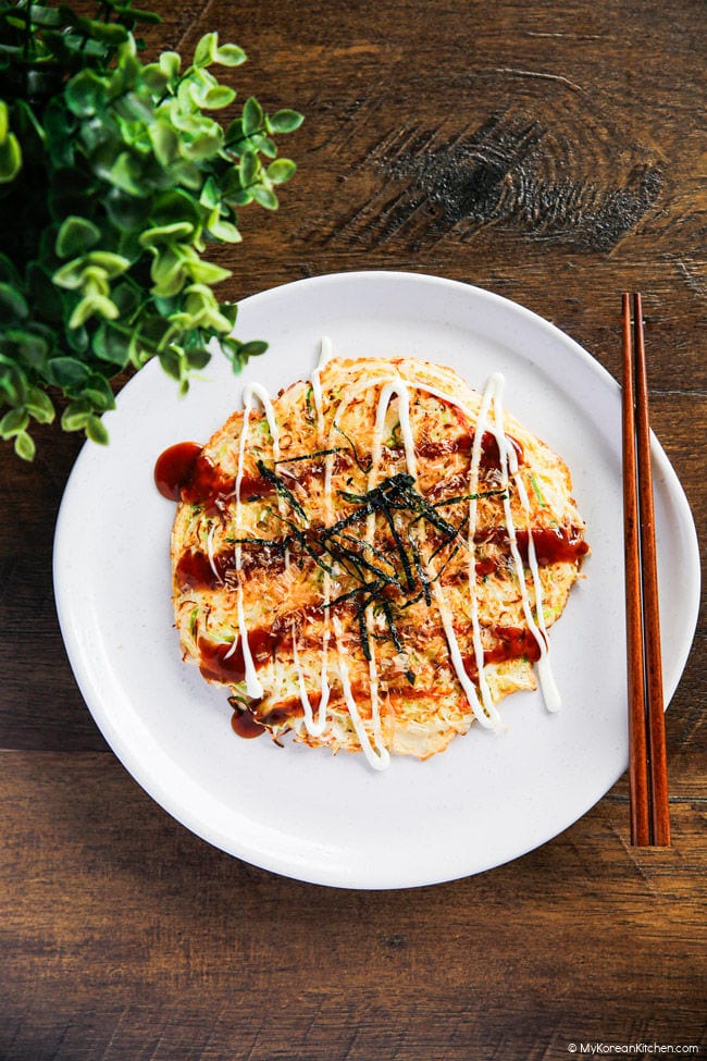 Cabbage and egg omelette with sauce served on a white plate, wooden backdrop.