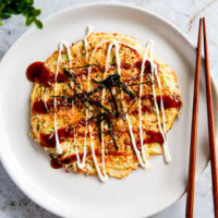 Cabbage and egg omelette with sauce served on a white plate, white bench top.