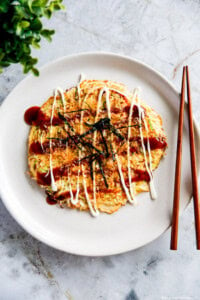 Cabbage and egg omelette with sauce served on a white plate, white bench top.