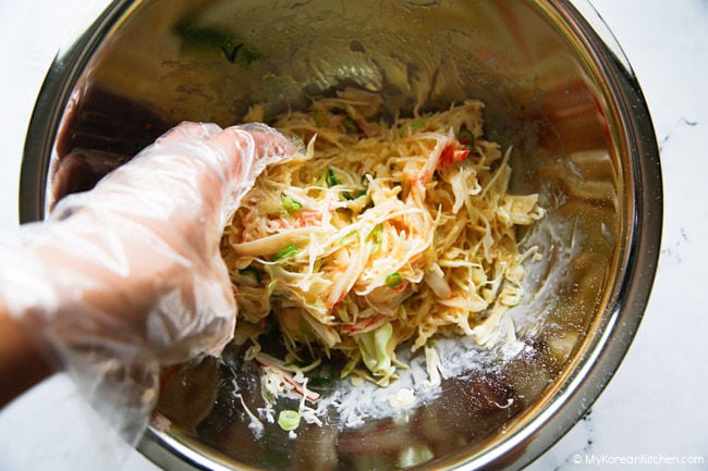 Hand in food glove mixing cabbage egg omelette ingredients in a stainless steel bowl.