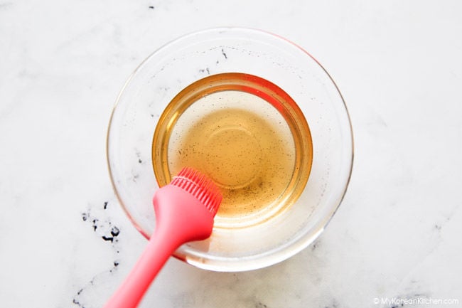 Vanilla syrup in a small glass bowl with a pink silicone brush for cake glazing.