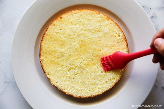 Applying vanilla syrup glaze to a sponge cake base.