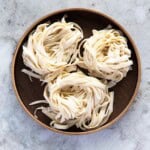 Three bundles of knife-cut noodles placed on a round wooden plate