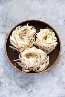Three bundles of knife-cut noodles placed on a round wooden plate