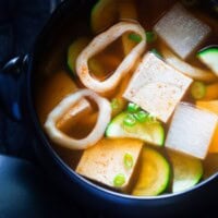 Bowl of Korean squid soup with tofu, vegetables, and squid rings.