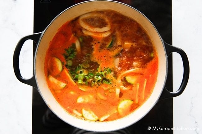 A pot of Korean squid soup with sliced squid rings, vegetables, and green onion.