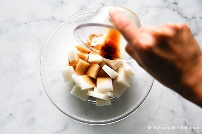 A person pouring marinade over thinly sliced radish in a mixing bowl.