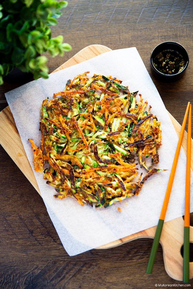 Golden, crispy Korean zucchini pancakes on a wooden cutting board lined with baking parchment, with a pair of chopsticks on top