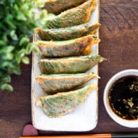 Pan-fried stuffed perilla leaves on a slim rectangular plate with chopsticks below and dipping sauce on the right