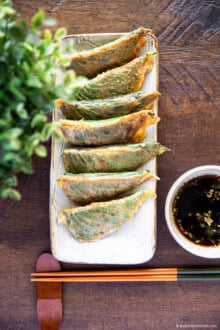 Pan-fried stuffed perilla leaves on a slim rectangular plate with chopsticks below and dipping sauce on the right