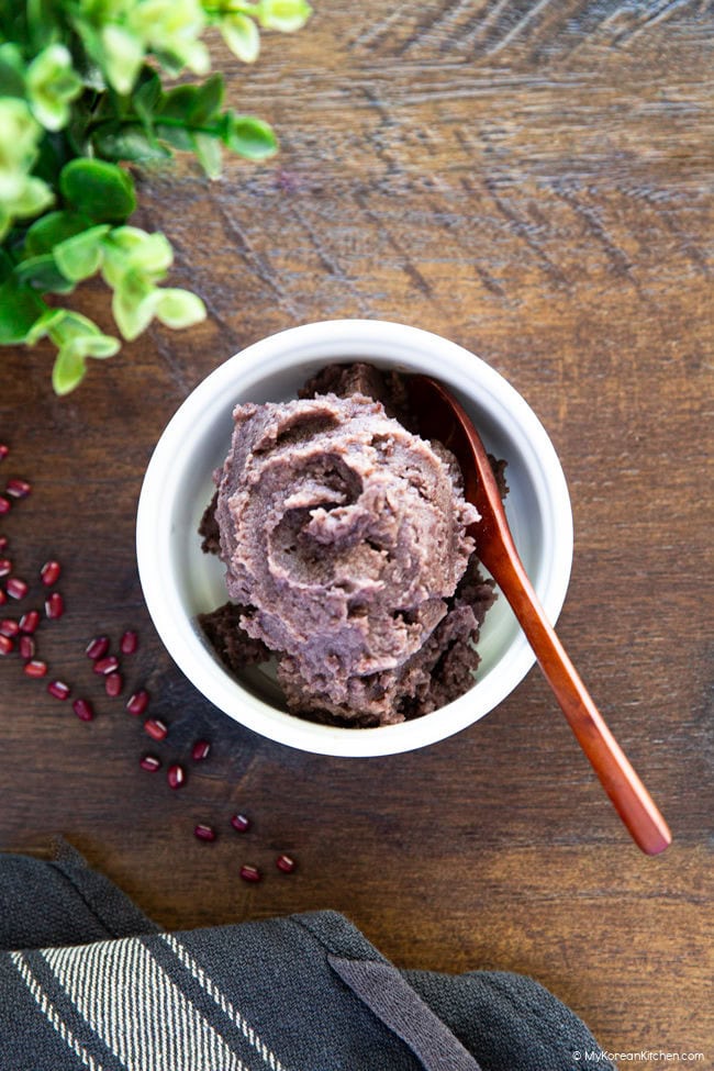 A bowl of sweet red bean paste with a wooden spoon, placed on a wooden board.