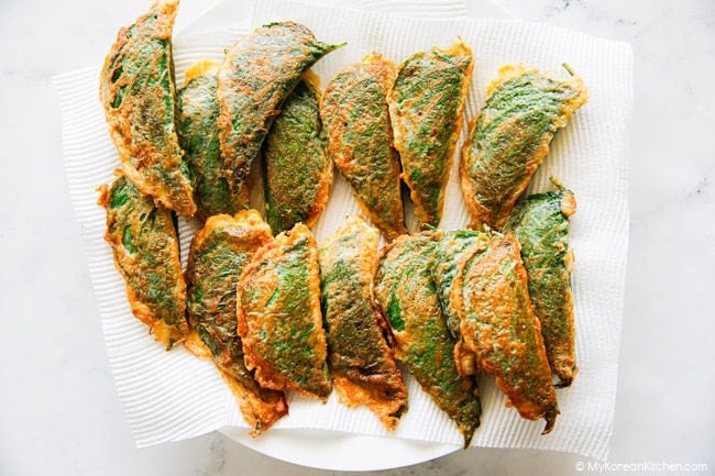 Pan-fried stuffed perilla leaf pancakes stacked on a large plate with kitchen paper