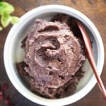 A close-up photo of a bowl of sweet red bean paste with a wooden spoon, placed on a wooden board.