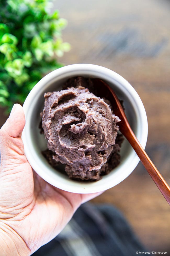 Holding a bowl of sweet red bean paste with a wooden spoon inside.